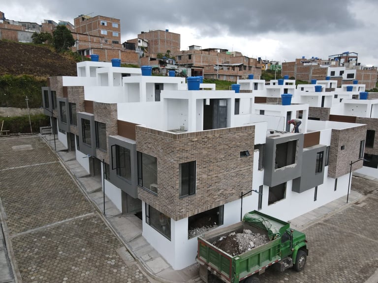 Modern multi-story residential buildings with white and brick facades in a hillside neighborhood under cloudy skies